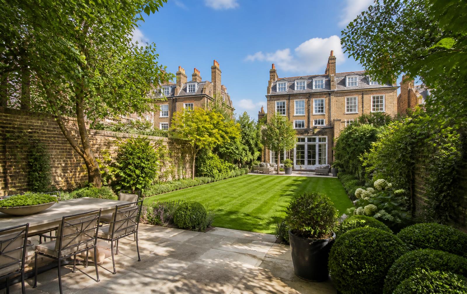 Private walled garden on a sunny day with a striped lawn and mature planting behind an elegant home